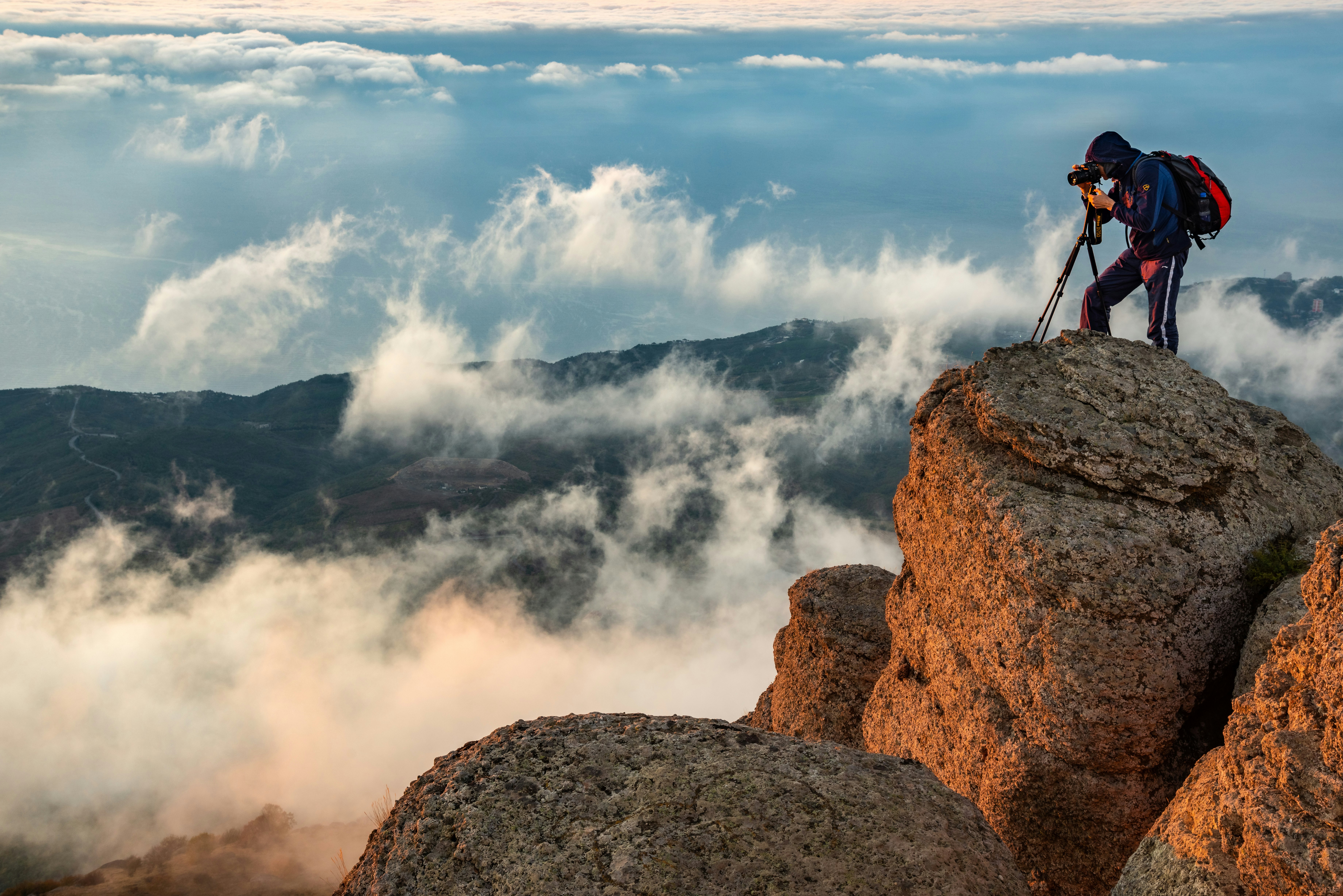 man in black jacket standing on brown rock formation under white clouds during daytime